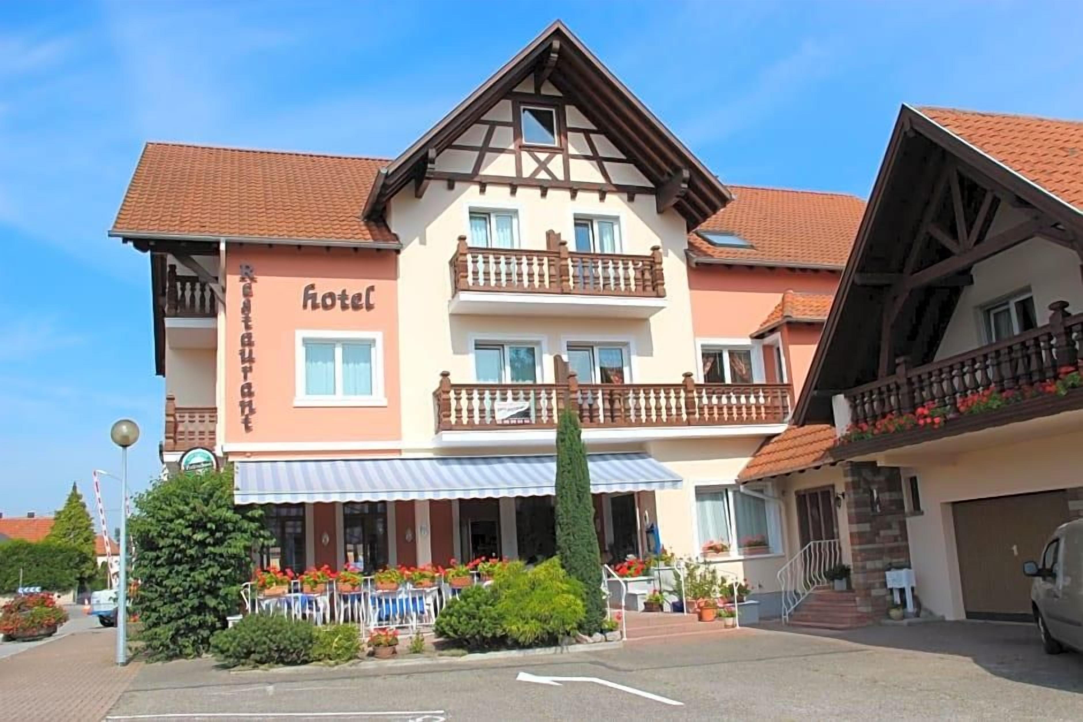 A two-story hotel with a balcony on the upper floor, a restaurant on the ground floor, and a parking area in front.