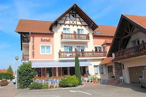 A two-story hotel with a balcony on the upper floor, a restaurant on the ground floor, and a parking area in front.