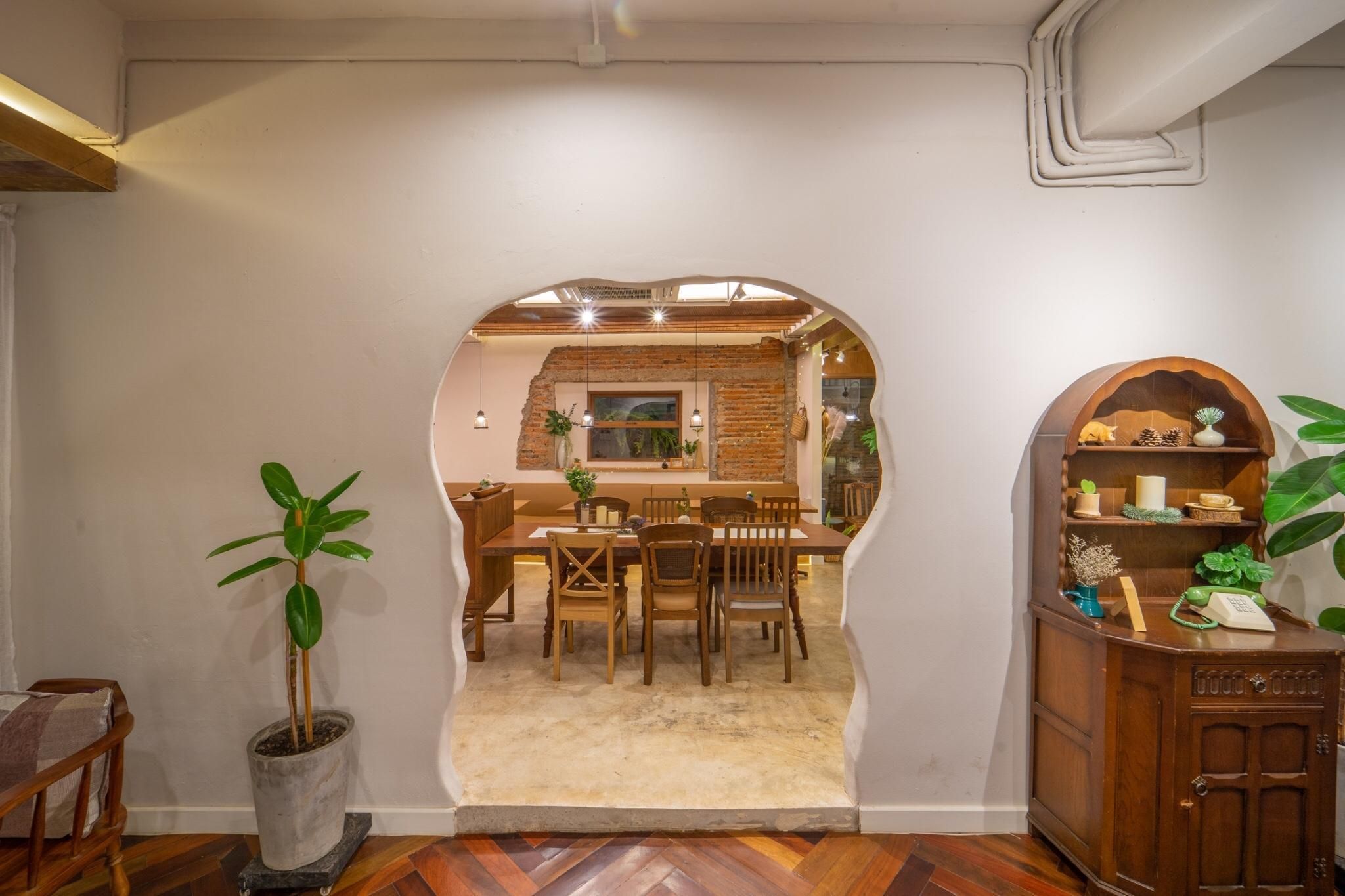 A dining area with a brick wall, wooden furniture, and a view into another room.