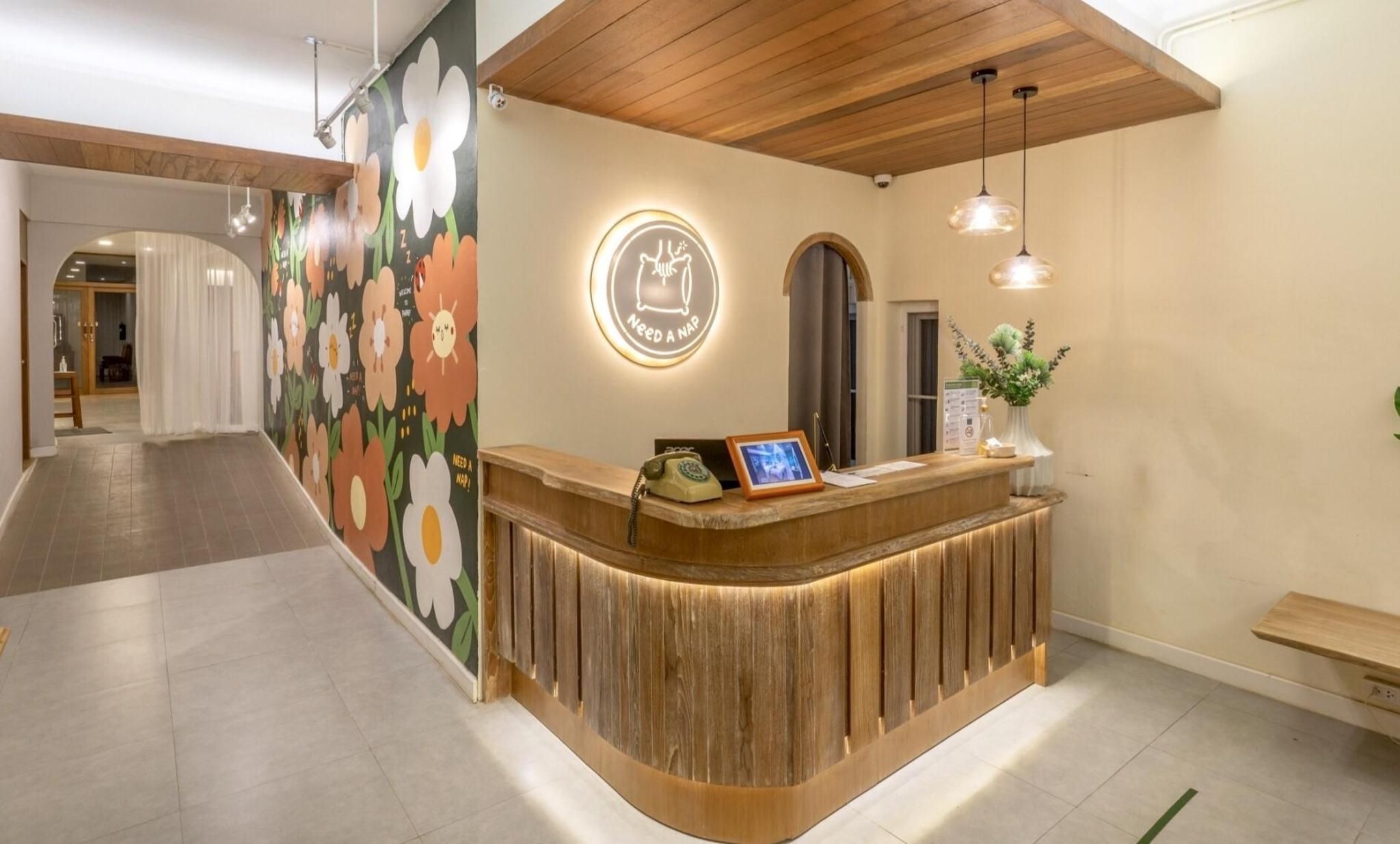 A reception desk with a wooden finish, a wall with a floral mural, and a circular sign with a nap symbol.