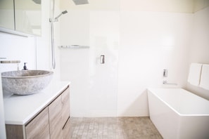 Un baño moderno con una bañera grande, un lavabo redondo de mármol y una ducha a pie.