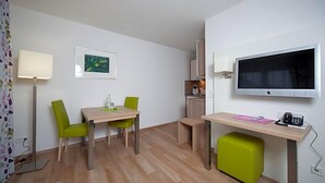 A compact room with a dining table, chairs, a small stool, a TV, and a desk with a phone. - Hotel Am Pan (Emmerich)