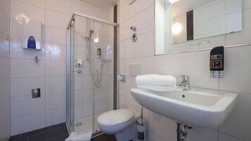 Een moderne badkamer met een glazen douchecabine, een witte wastafel en een toilet.