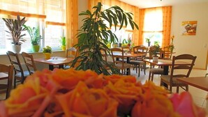 A dining area with multiple tables and chairs, potted plants, and a large central plant. - Hotel Am Pan (Emmerich)