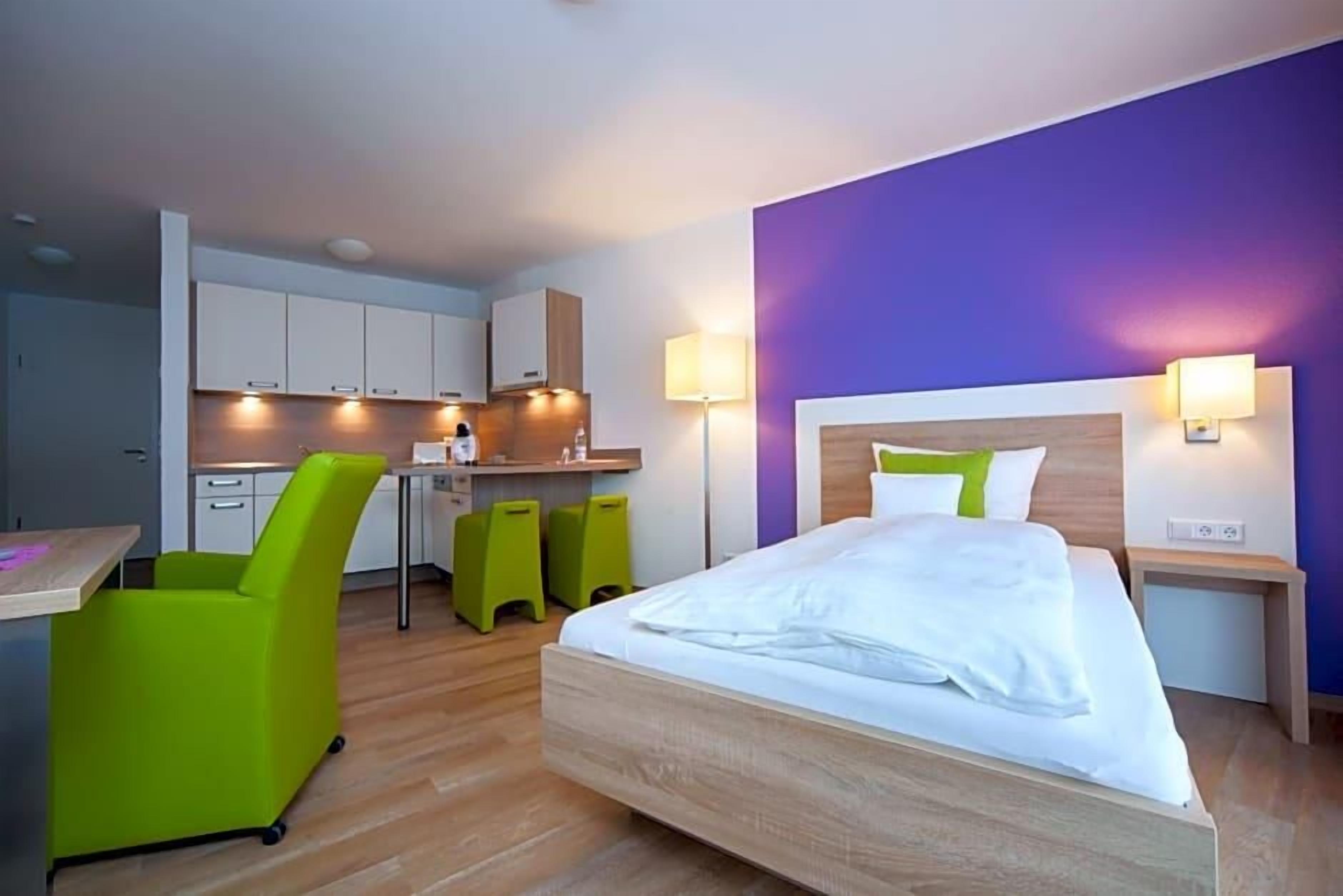Una habitación de hotel con cama, escritorio, silla y kitchenette.