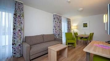 Een woonkamer met een bank, een klein houten tafeltje, een eettafel met stoelen en een lamp.