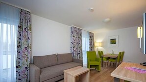 A living room with a sofa, a small wooden table, a dining table with chairs, and a lamp. - Hotel Am Pan (Emmerich)