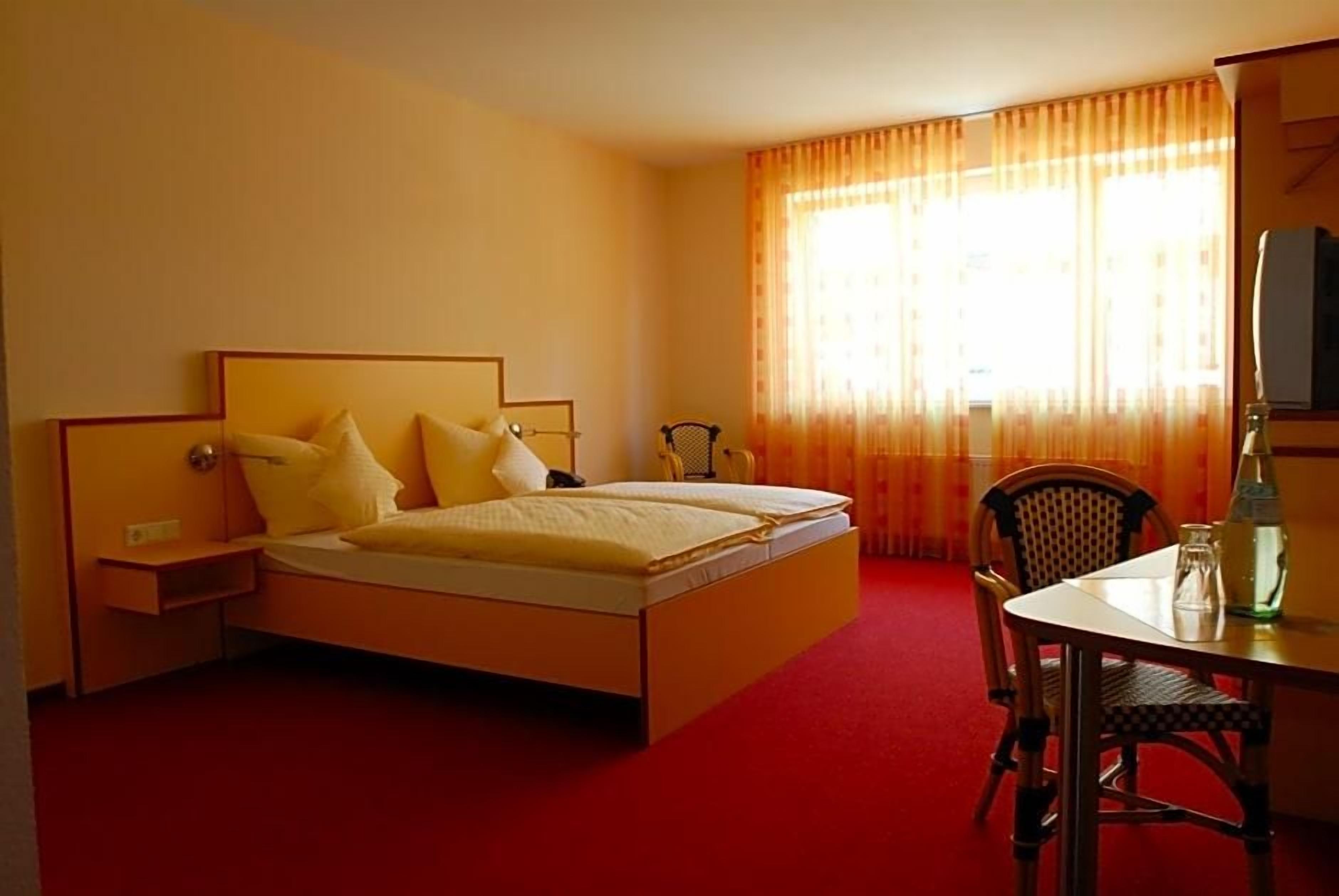 A hotel room with a bed, a chair, a table, and a television.