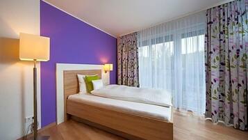 Een hotelkamer met een bed, nachtkastje, lamp en raam met gordijnen.