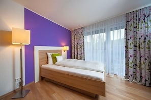 Quarto de hotel com cama, mesa de cabeceira, luminária e janela com cortinas.