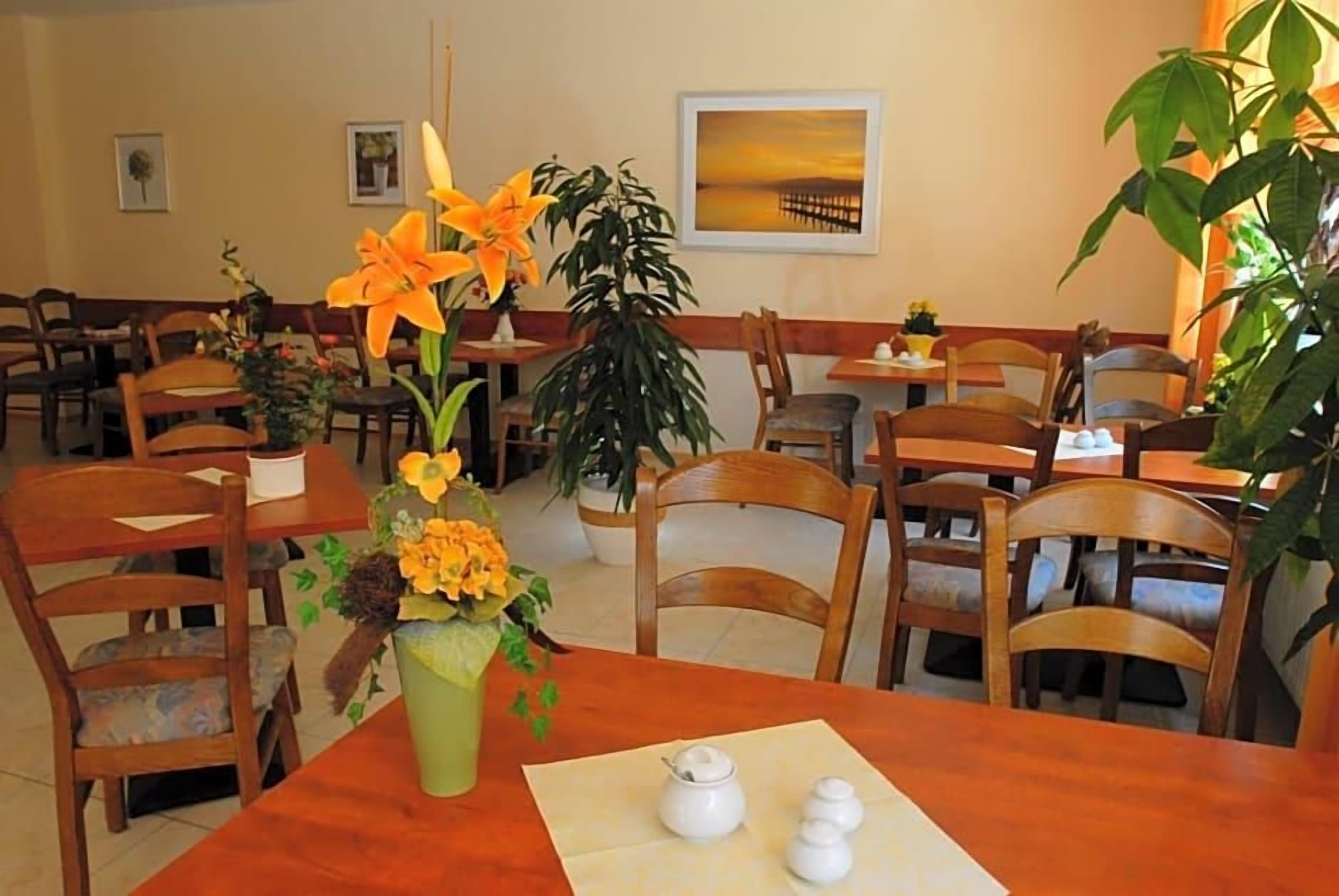 Ein Essbereich mit Holztischen und -stühlen, einer Blumenvase und einem Bild an der Wand.