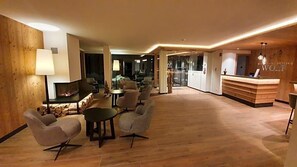 A modern hotel lobby with a reception desk, seating area, and a fireplace. - Hotel Wolf (Selva di Val Gardena)