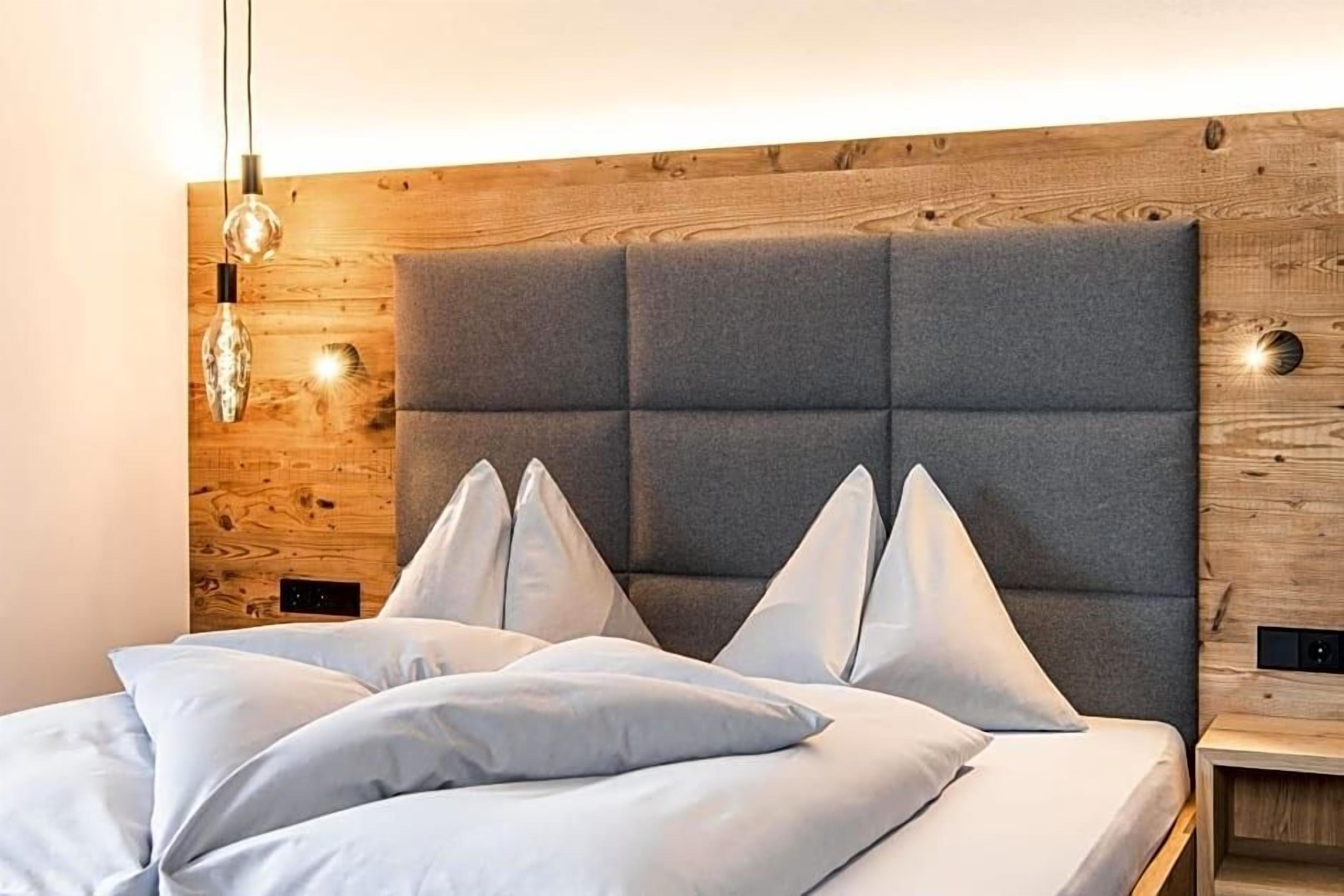 Een bed met een grijs gestoffeerd hoofdbord, witte kussens en een houten paneel.