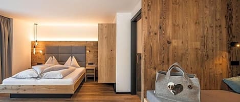 A modern bedroom with a wooden floor, a bed with a grey headboard, and a grey sofa with a heart-shaped pillow.