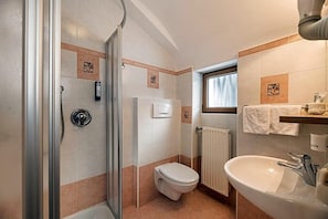 A bathroom with a glass shower enclosure, a toilet, a sink, and a window providing natural light. - Hotel Wolf (Selva di Val Gardena)