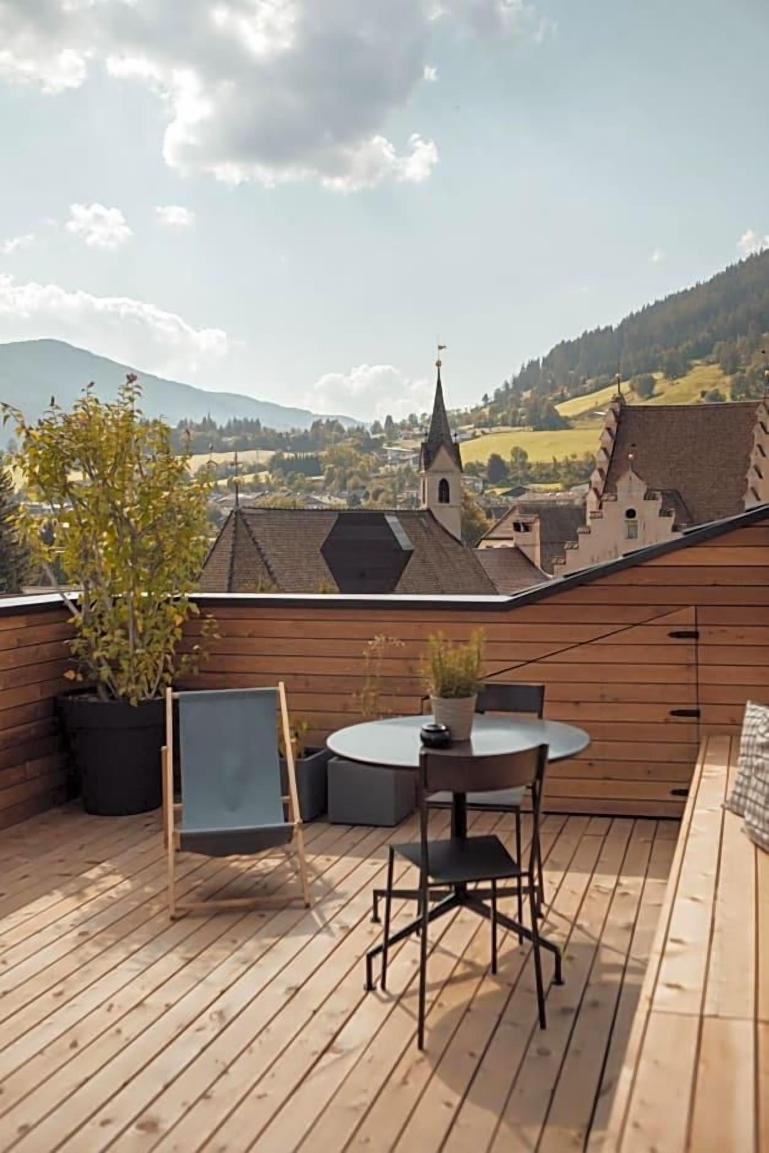 A wooden deck with a table and chairs, overlooking a village with a church and houses.