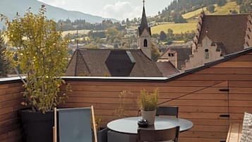Um deck de madeira com mesa e cadeiras, com vista para uma aldeia com igreja e casas.
