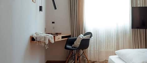 Habitación de hotel con cama, escritorio, silla, lámpara y ventana con cortinas.