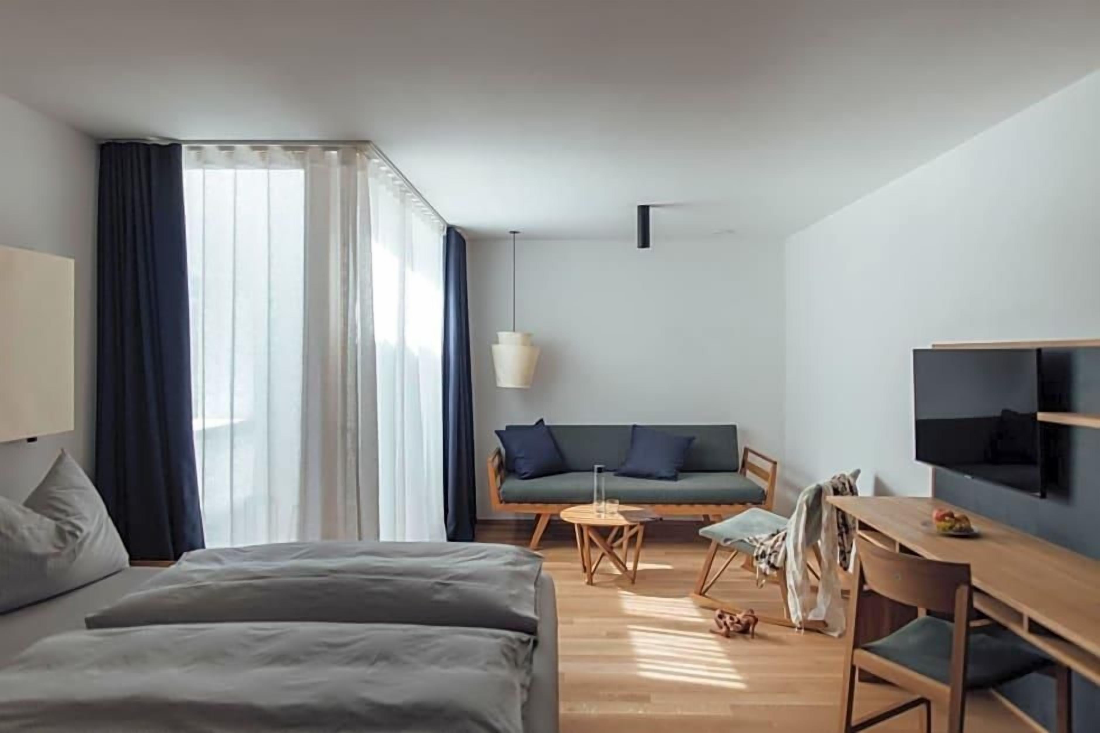 Quarto de hotel moderno com cama, sofá, mesa de jantar e televisão.