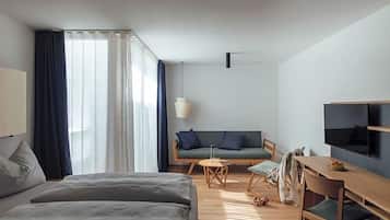 Quarto de hotel moderno com cama, sofá, mesa de jantar e televisão.
