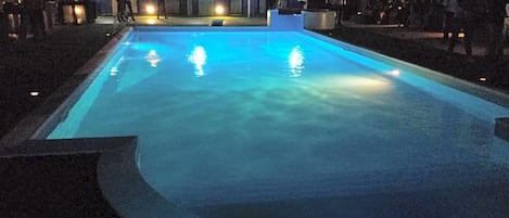 A swimming pool at night with a curved edge and a small seating area.