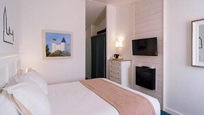 Une chambre d’hôtel avec un lit, un téléviseur fixé au mur, un tableau encadré et une fenêtre avec des rideaux.