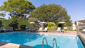 Une piscine entourée d’arbres et d’une clôture, avec des chaises longues et des parasols.