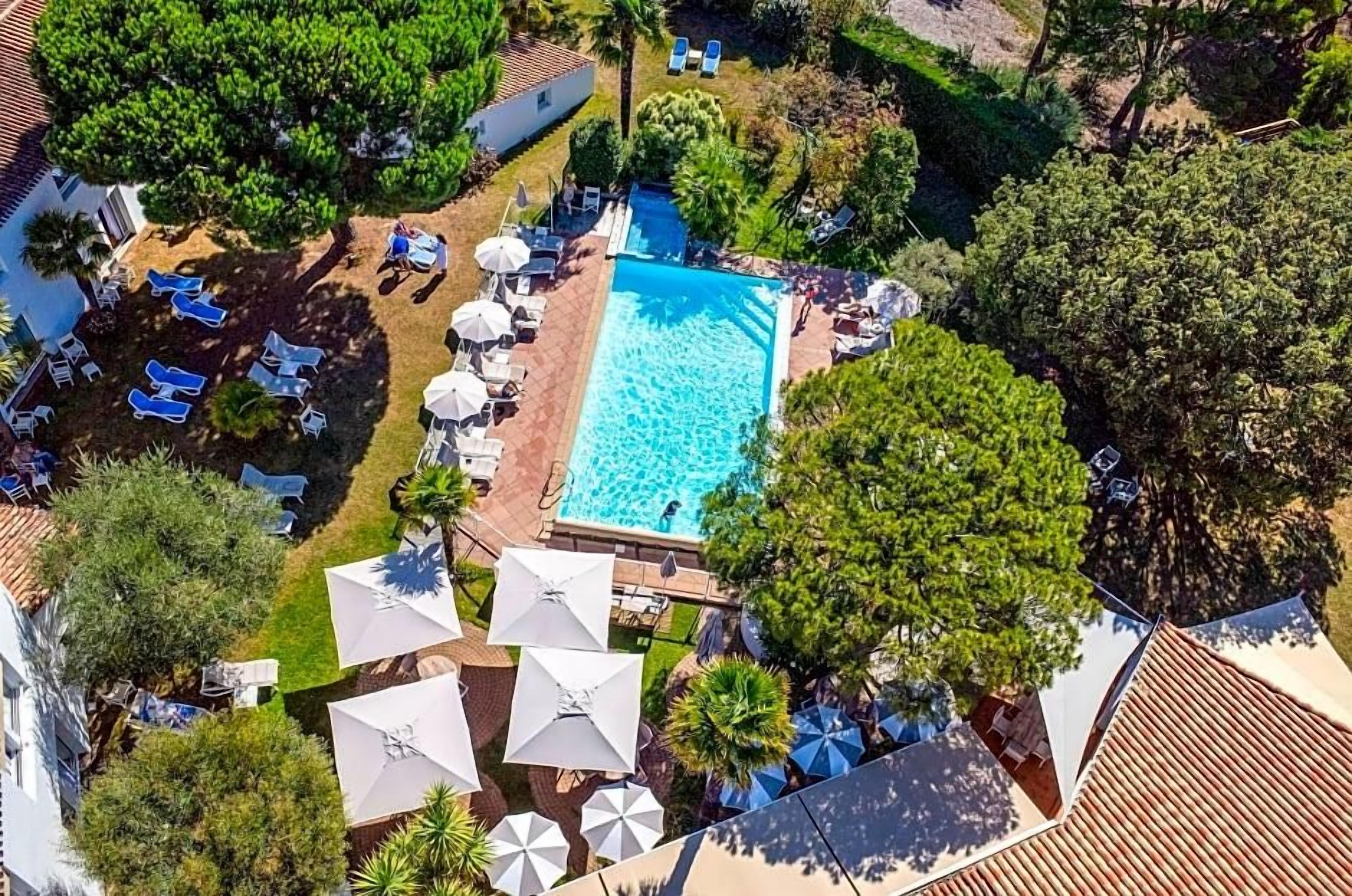 Vista aerea di un resort con piscina circondata da poltrone a sdraio e ombrelloni.