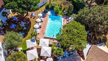 Vue aérienne d’un complexe hôtelier doté d’une piscine, entourée de chaises longues et de parasols.