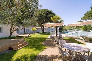 Un patio con mobiliario exterior, una piscina y un edificio al fondo.