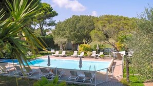Une piscine entourée de verdure et d’arbres, avec des chaises longues et des parasols.