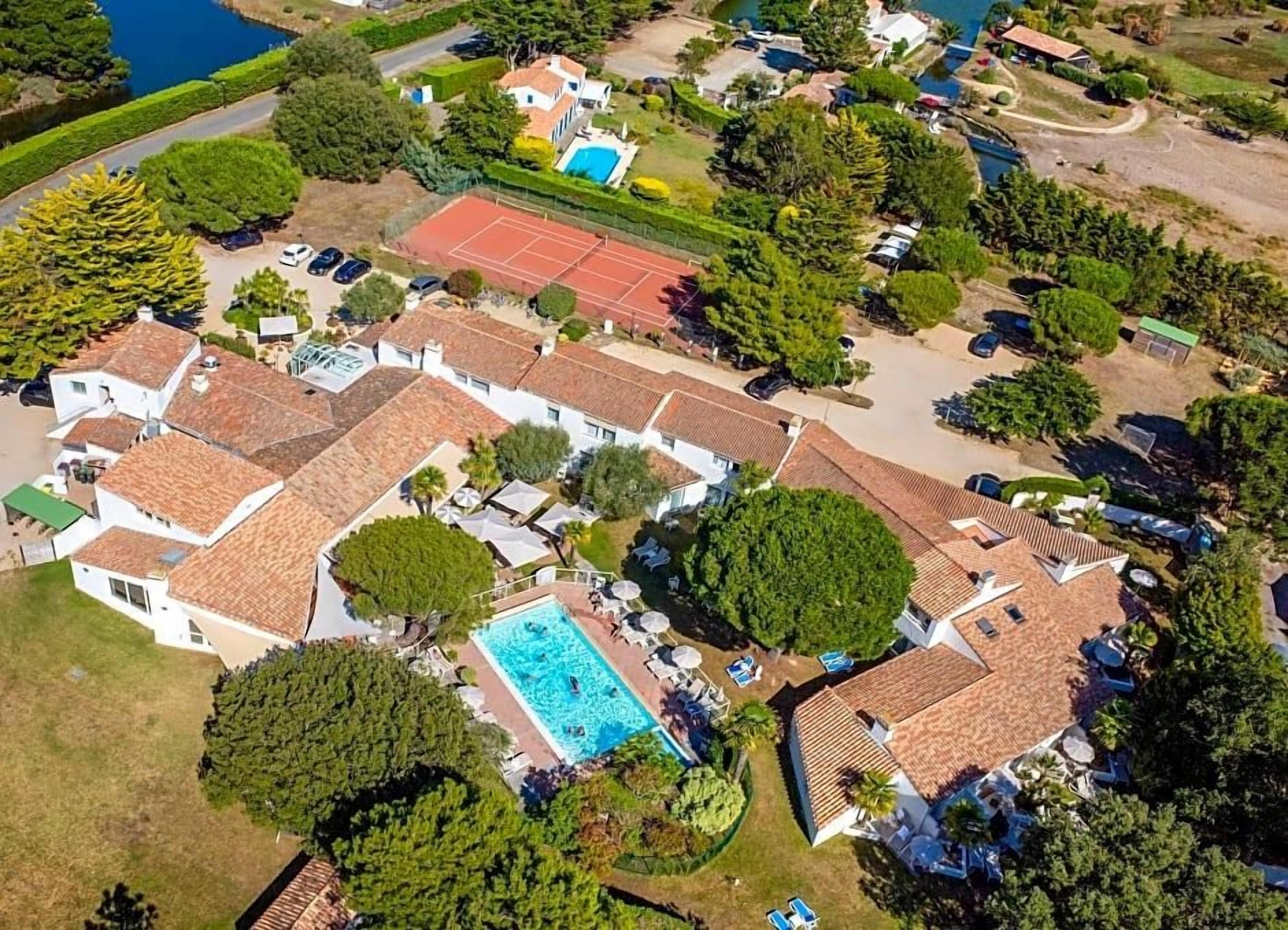 Un quartier résidentiel comprenant plusieurs maisons, une piscine, des courts de tennis et une végétation luxuriante.