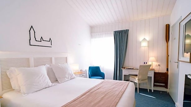 Une chambre d’hôtel comprenant un lit, un bureau, une chaise, une lampe et une œuvre d’art accrochée au mur.