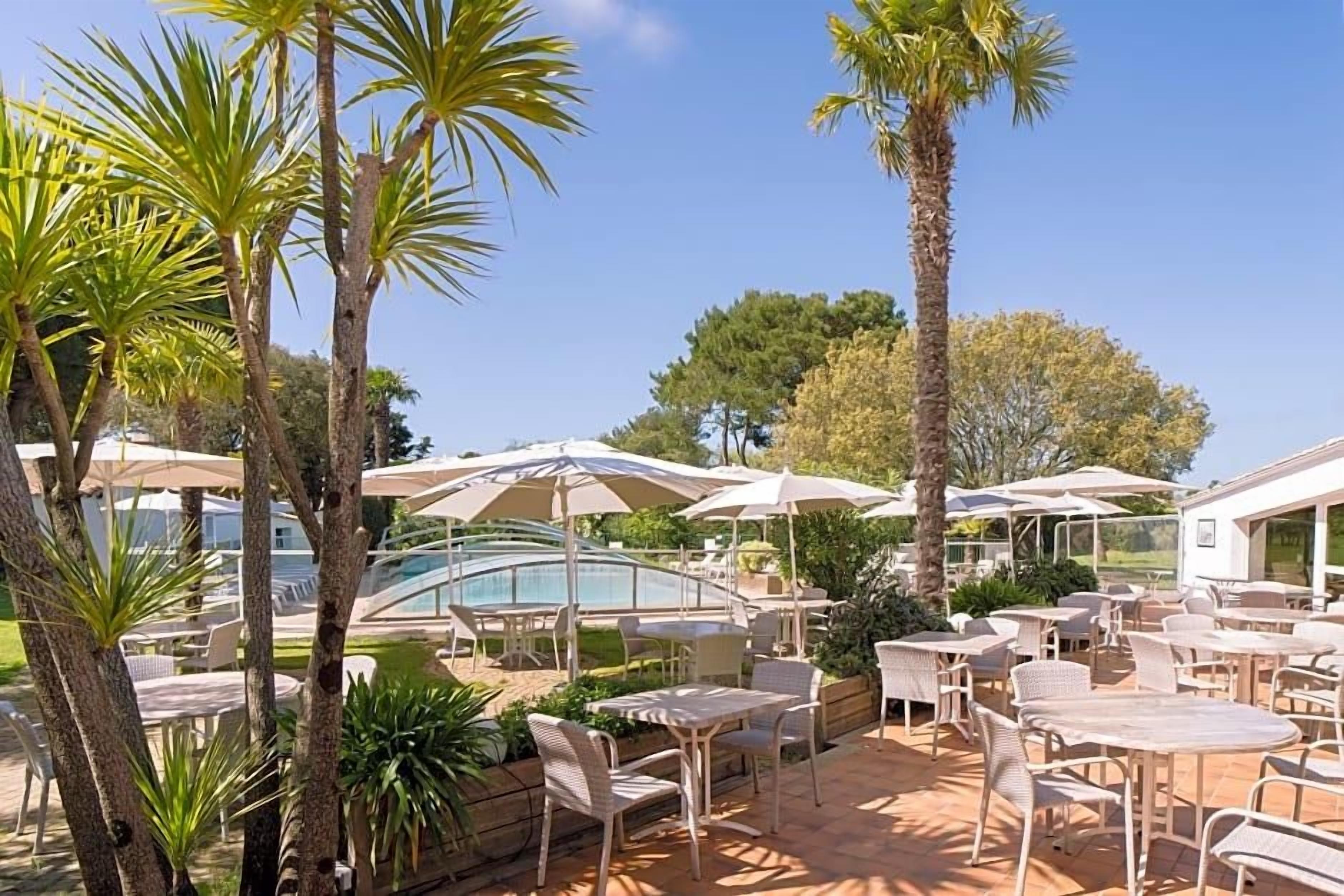 Un espace extérieur aménagé en terrasse, avec des tables et des chaises, des parasols et une piscine.
