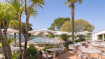 Un espace extérieur aménagé en terrasse, avec des tables et des chaises, des parasols et une piscine.