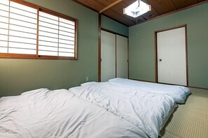 Ein Zimmer mit zwei Betten, einem Fenster mit Jalousien und einer Tür.