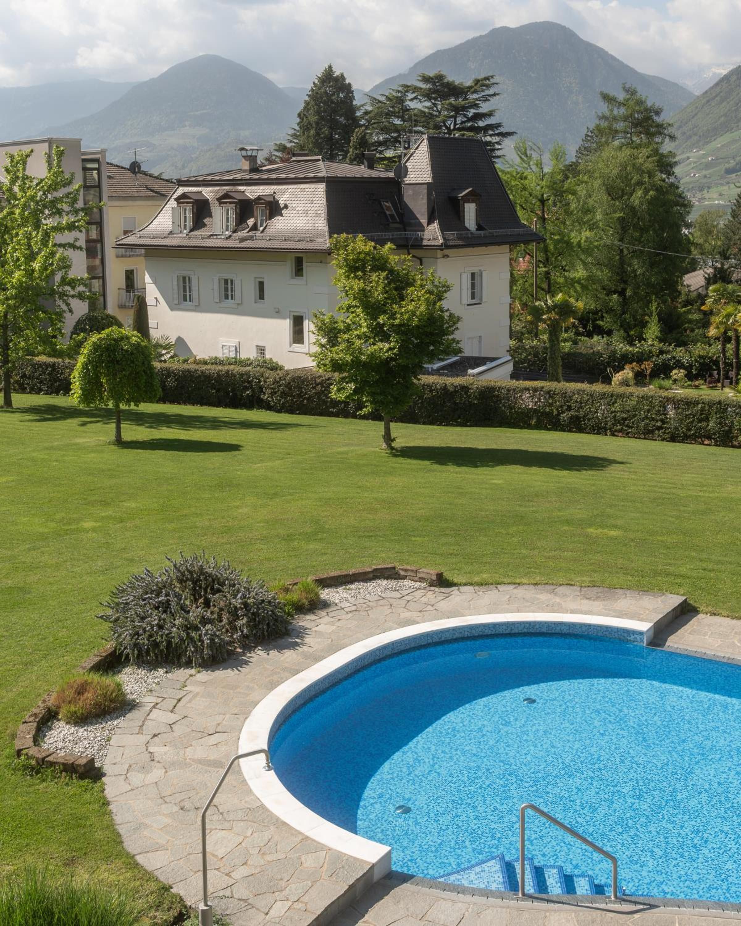 A residential property with a swimming pool, a well-maintained lawn, and a view of mountains in the background.
