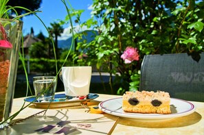 A table with a plate of food, a glass of water, and a white mug, set outdoors with greenery and a flower in the background. - Hotel Filipinum (Merano)