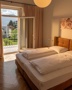 A bedroom with a bed, a nightstand, a lamp, and a view of the outdoors through a sliding door. - Hotel Filipinum (Merano)