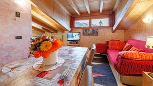 A cozy room with a wooden ceiling, a television, a sofa, and a table with a floral arrangement. - Hotel San Rocco (Livigno)