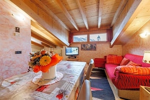 Una habitación acogedora con techo de madera, un televisor, un sofá y una mesa con un arreglo floral.