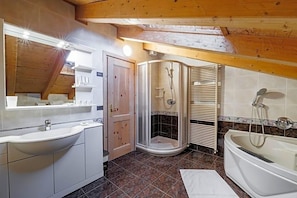 Un baño con lavamanos, ducha y bañera, vigas de madera en el techo y suelo de baldosas.