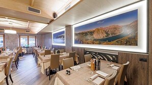A restaurant with wooden interiors, multiple dining tables, and large landscape paintings on the walls. - Hotel San Rocco (Livigno)