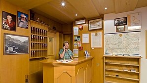 A reception desk with a wooden counter, framed photographs, a map, and various notices on the wall. - Hotel San Rocco (Livigno)