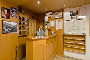 Un mostrador de recepción con encimera de madera, fotografías enmarcadas, un mapa y varios avisos en la pared.