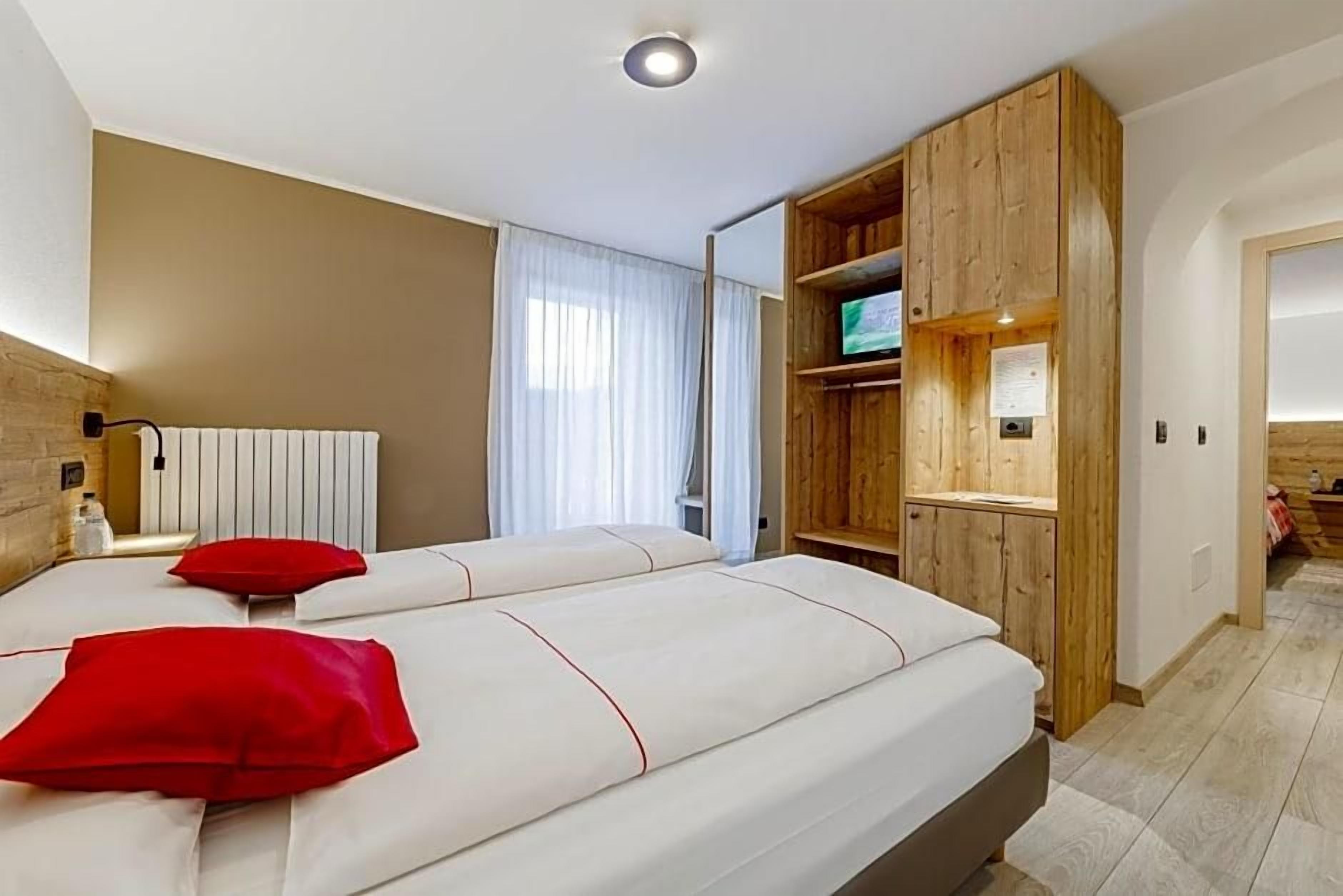 A hotel room with two beds, a wooden wardrobe, a television, and a radiator.