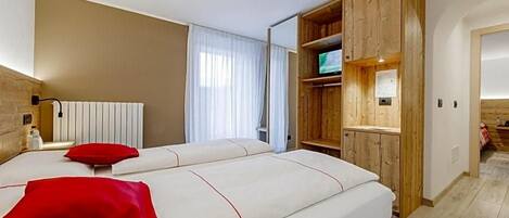 A hotel room with two beds, a wooden wardrobe, a television, and a radiator.
