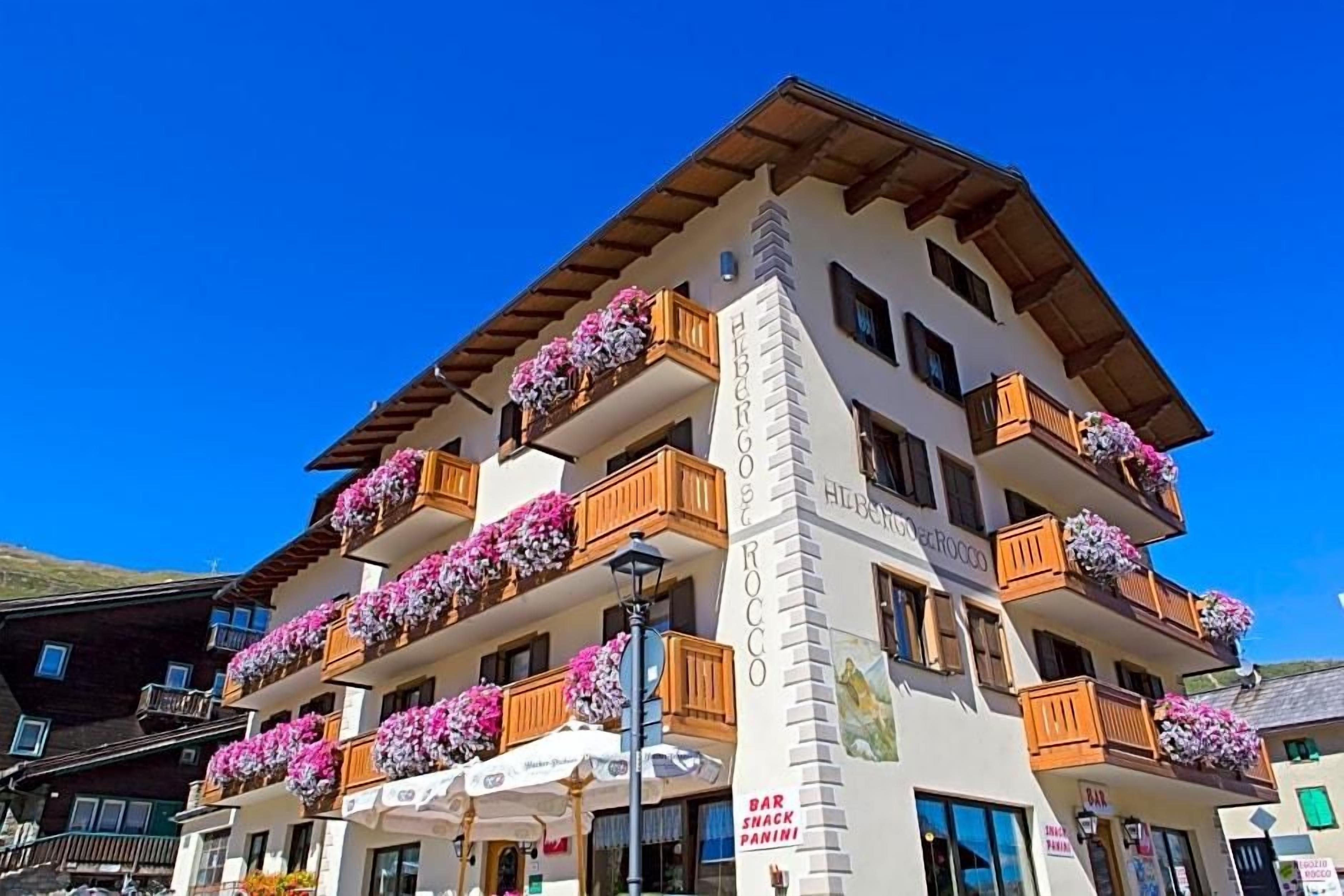 A multi-story hotel with balconies adorned with flowers, a bar, and a restaurant.