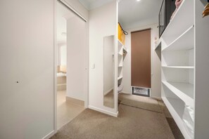 A hallway with a white door leading to a bathroom, a staircase, and a closet with shelves. - Waters Edge Twin Waters - Pool, Deck & Kayaks (Coolum Region)