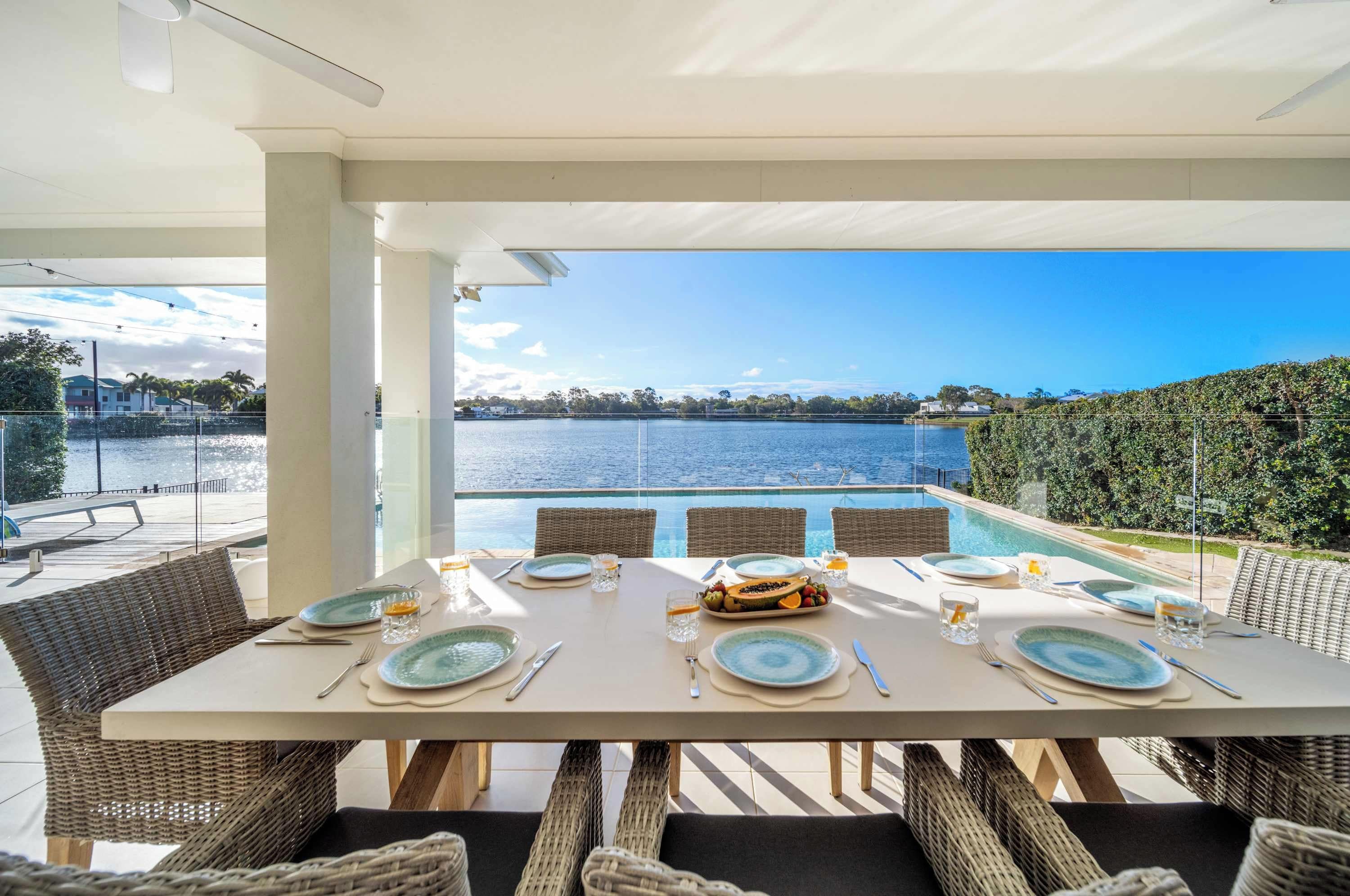 A dining table set for six with a view of a lake and a clear sky.